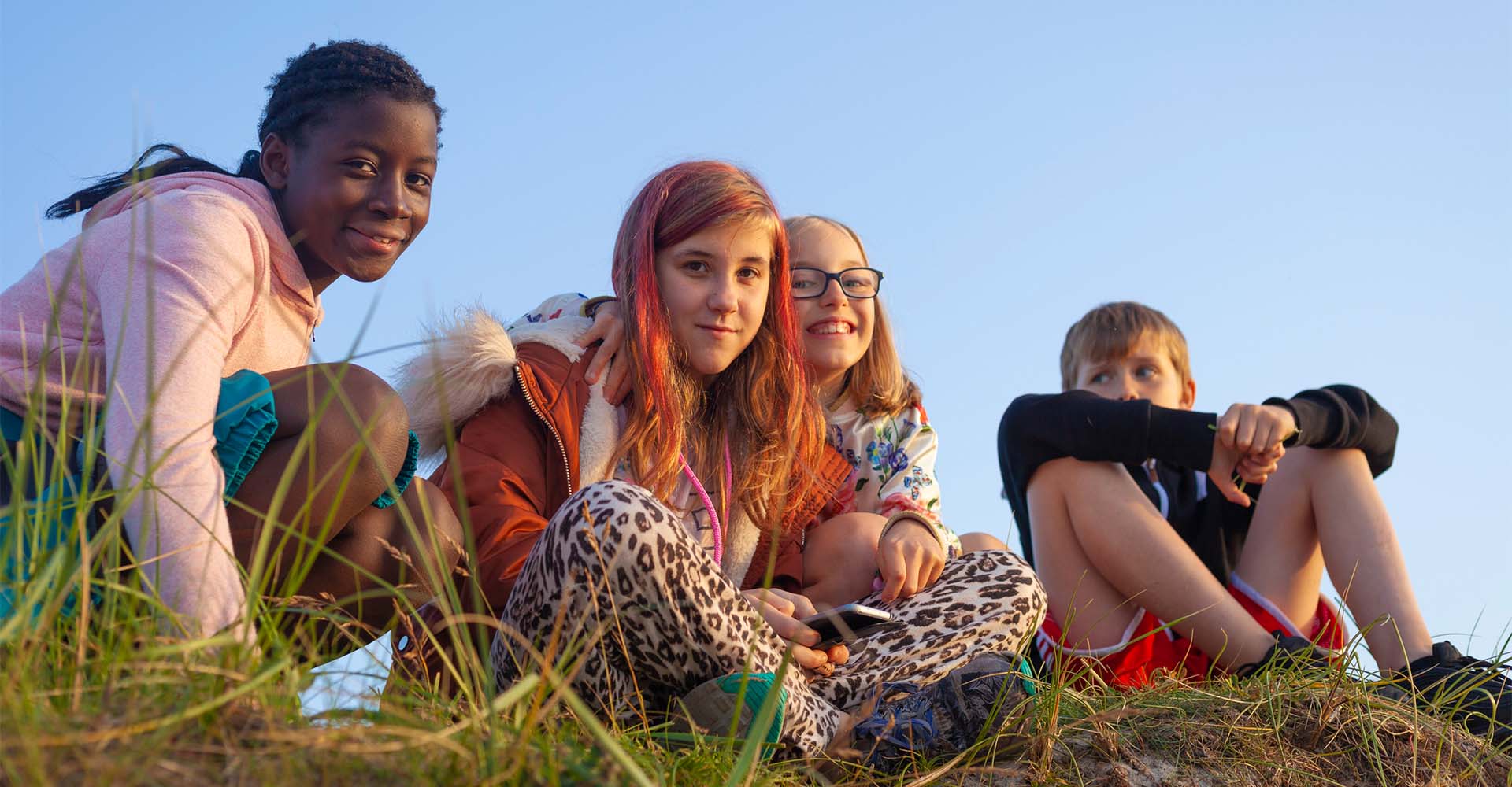 Kinder die zusammen in der Natur Zeit verbringen und mittags auf einer Sanddüne im Gras sitzen.