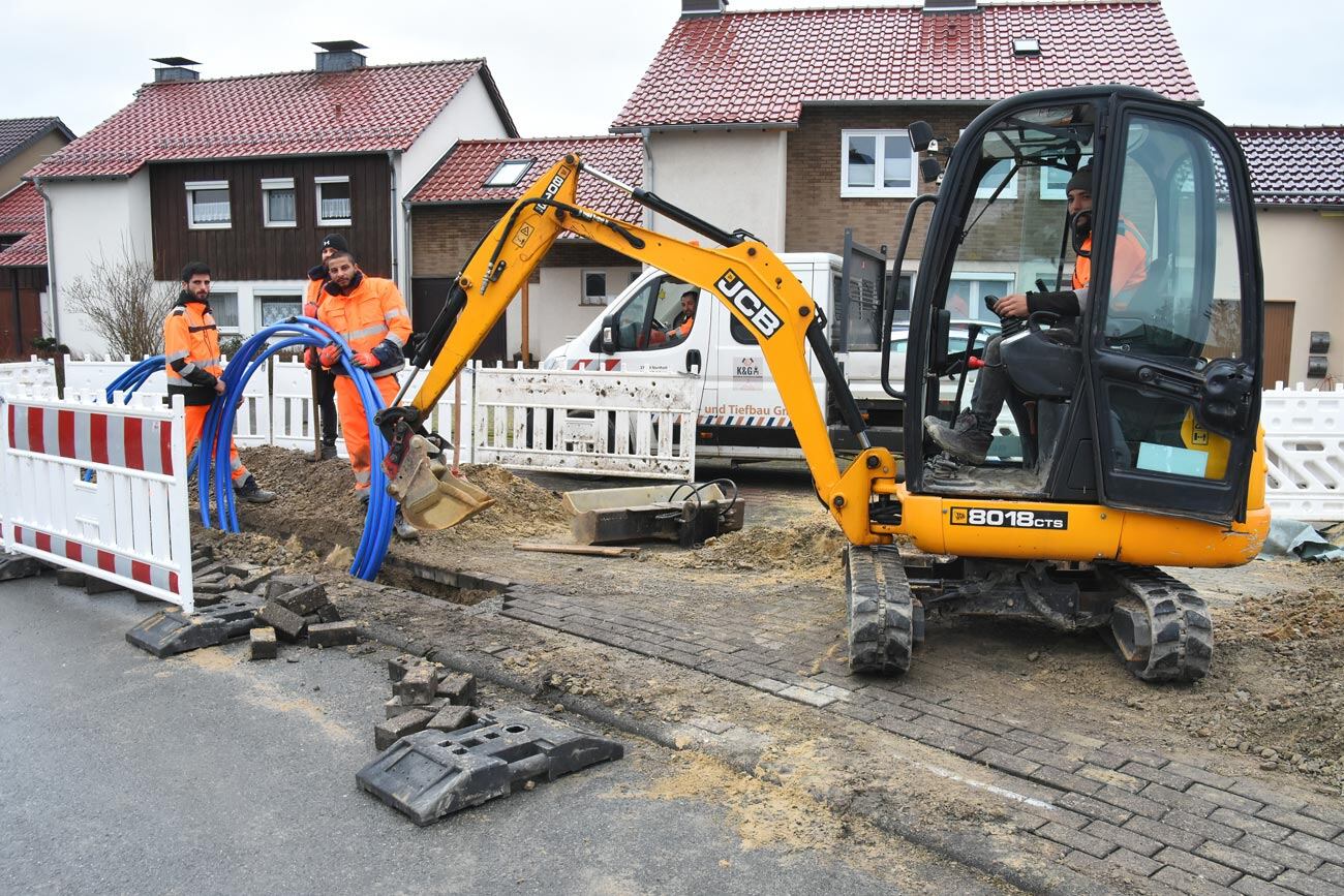 Arbeiter verlegen Glasfaserkabel auf einer Baustelle in Brakeler Ortschaft mit Hilfe eines Baggers