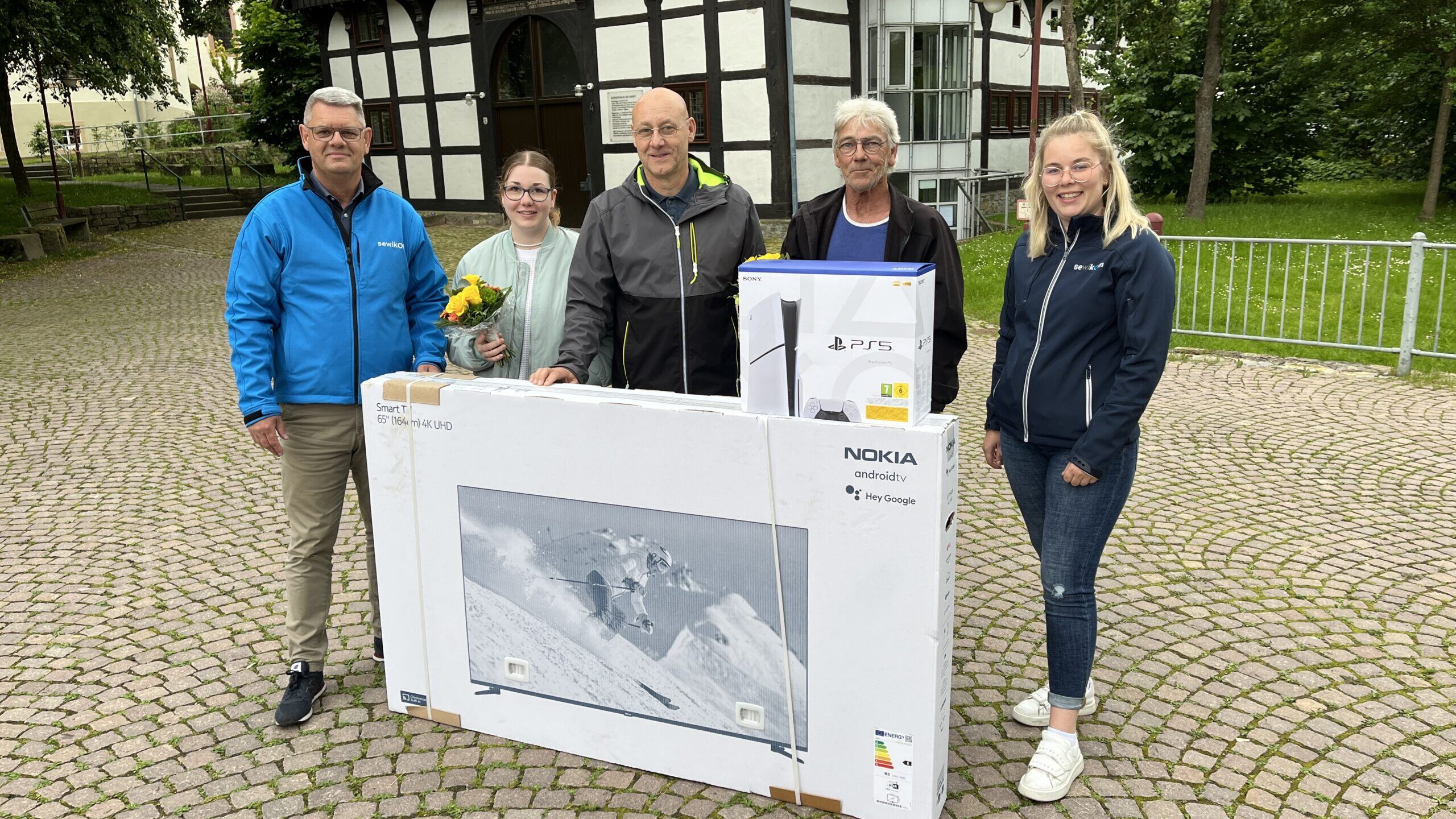 Fünf Personen stehen mit einem gewonnenen Fernseher und einem Blumenstrauß in Kalletal