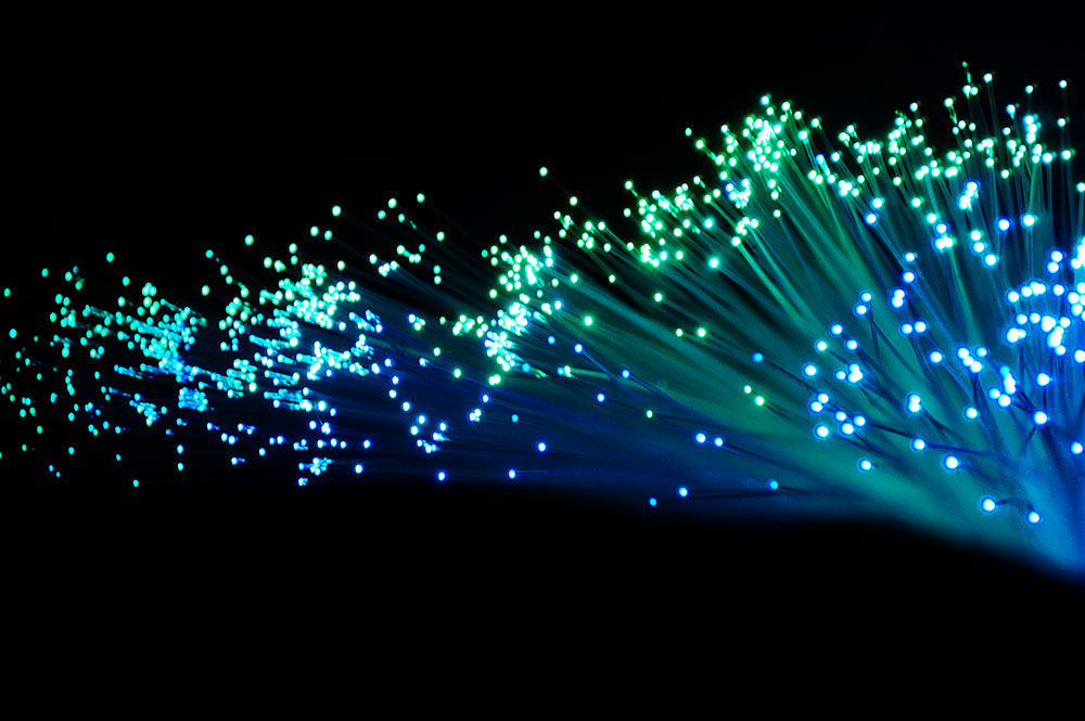 Optische Fiber Kabel die grün, blau leuchten und vor einem schwarzen Hintergrund liegen.